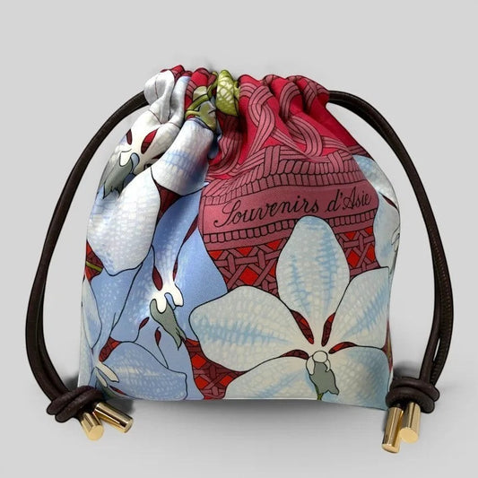 Prettysac Souvenirs D'Asie floral print drawstring pouch with sky blue, white, and crimson orchids and geometric patterns. Features dark brown cords and gold hardware.