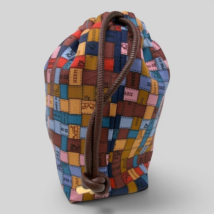 Prettysac Hermes Paris silk blend drawstring pouch with patchwork of equestrian motifs and 'Hermès-Paris' stamps in earthy tones and pastels.